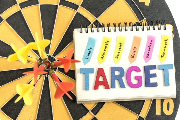 six dart in bullseye with words target on the notebook with handwriting timely achievable relevant goals education teamwork over dartboard background, Business success concept